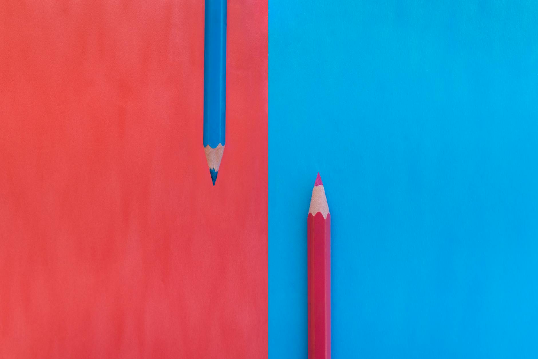 A creative flat lay of red and blue pencils with matching colored backgrounds, showing contrast and symmetry.