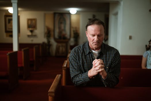 Adult man kneeling in church pew, praying with devotion in a quiet, sacred setting.